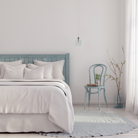 Quarto pintado de branco com cama e almofadas brancas com uma cadeira azul