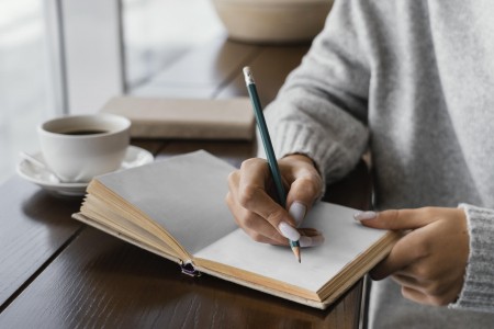 Uma rapariga a escrever no seu caderno com um lápis e chávena ao lado